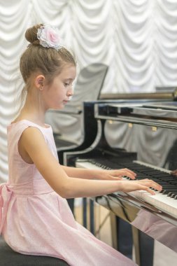 üzerinde siyah bir grand piyano güzel pembe elbiseli kız. Üzerinde siyah bir piyano çalan kız. Dikey fotoğraf.