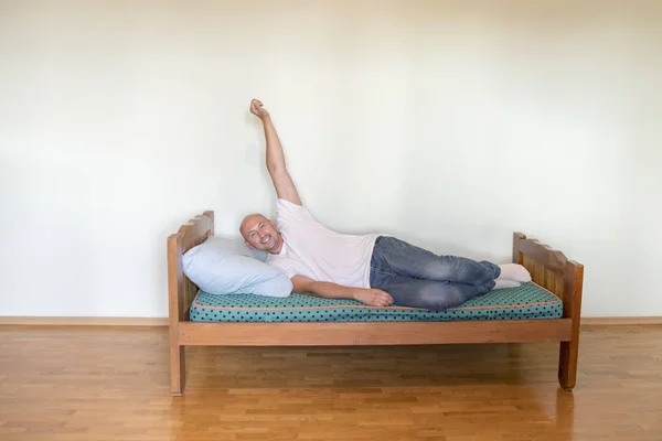 A happy man on a bed in an empty room. The concept of asceticism makes a person happy.