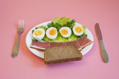 Kahvaltı. Haşlanmış yumurta, pastırma, pembe bir arka plan üzerinde beyaz bir tabak içinde ekmek Yeşiller.