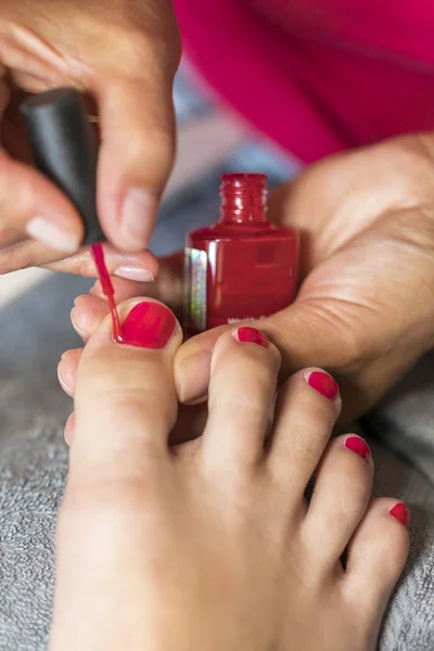 女性の足の爪を気に手袋の手 ペディキュア マニキュア美容サロン コンセプト 爪の赤い色でニスを塗るします 垂直写真 — ストック写真