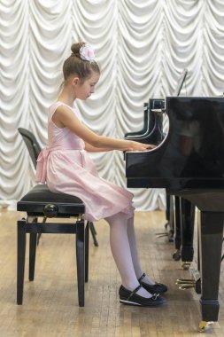üzerinde siyah bir grand piyano güzel pembe elbiseli kız. Üzerinde siyah bir piyano çalan kız. Dikey fotoğraf.