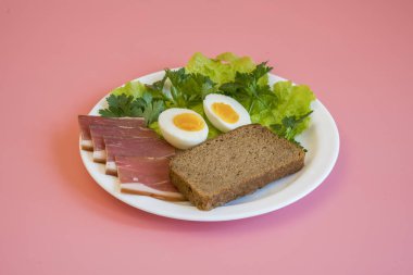 Kahvaltı. Haşlanmış yumurta, pastırma, pembe bir arka plan üzerinde beyaz bir tabak içinde Yeşiller.
