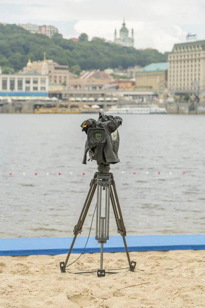 Television camera on the river beach. Lonely camcorder on a tripod. Vertical photo.