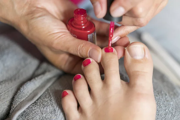 Hands in gloves cares about a woman\'s foot nails. Pedicure, manicure beauty salon concept. Nail varnishing in red color