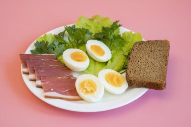 Kahvaltı. Haşlanmış yumurta, pastırma, pembe bir arka plan üzerinde beyaz bir tabak içinde Yeşiller.