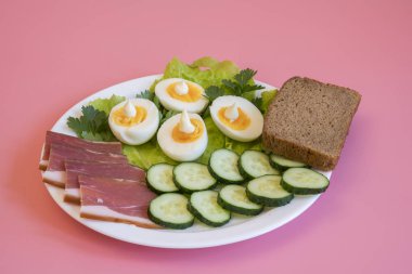 Kahvaltı. Haşlanmış yumurta, pastırma, pembe bir arka plan beyaz bir tabağa yeşillik. Gıda pembe bir arka plan üzerinde beyaz plaka.
