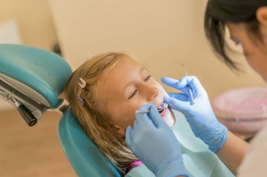 Küçük kız dişçi ofisinde resepsiyonda. sonra diş tedavileri diş hekimi yakın bir sandalyede oturan küçük kız. Diş hekimleri Office küçük kız sitts