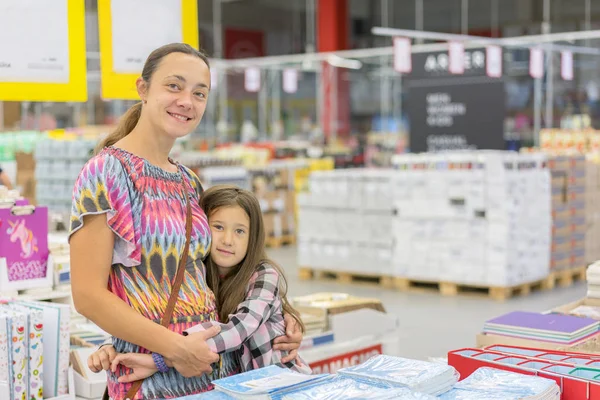 Hermosa mujer con una hija en un centro comercial. Mamá e hija en el supermercado. La hija abraza suavemente a su madre en el centro comercial — Foto de Stock