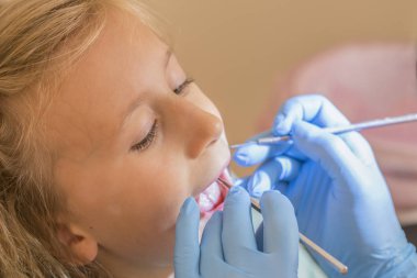 Elleri tanınmaz Pediatrik Diş hekimi hastane sandalyede oturan gülümseyen sevimli küçük kız için muayene yordam yapmadan. Diş hekimi ofisi. Küçük kız dişçi ofisinde oturuyor. yakın çekim.