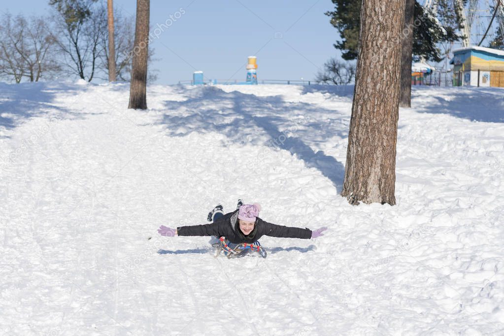 Young woman sledding in snow. laughing girl in winter clothing goes down on sleds down the hill.