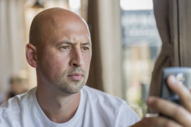 Düşünceli bir yaz kafede öğle yemeği sırasında oturan bir harf için bir akıllı telefon ekranında görünen kel adam. kafede çalışan iş adamı.