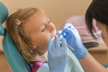 Elleri tanınmaz Pediatrik diş hekimi hastane sandalyede oturan gülümseyen sevimli küçük kız için muayene yordam yapmadan. Diş hekimi ofisi. Küçük kız dişçi ofisinde oturuyor.