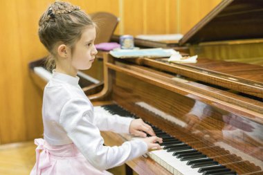 Güzel elbiseli bir kız üzerinde kahverengi bir kuyruklu piyano çalış