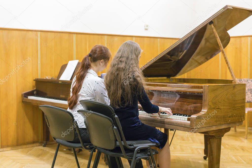 Two girls playing the piano. back view.