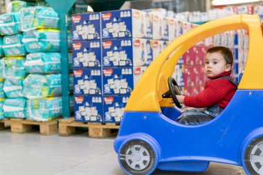kırmızı kazaklı çocuk bezi bir arka plan üzerinde bir alışveriş merkezinde bir çocuk arabada küçük bir neşeli çocuk