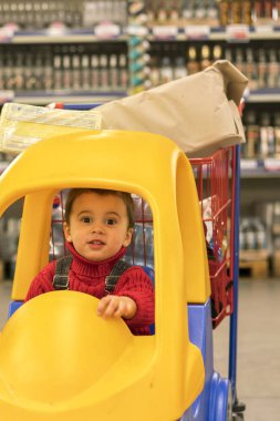 Yürümeye başlayan çocuk ters bir alışveriş merkezinde bir bebek arabası içinde alkol ile şişe.