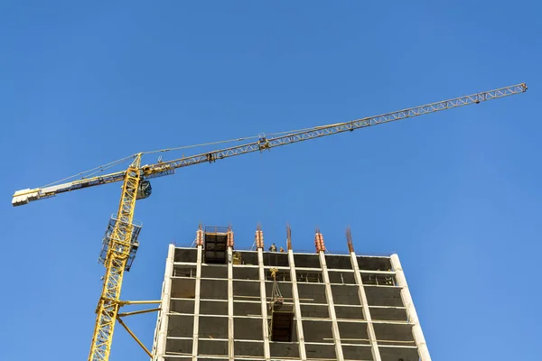 Construction of a high-rise building. Crane, builders against the blue sky.