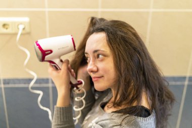 Elektrik blowdryer evde saç kurutma kahverengi saçlı genç kadın.