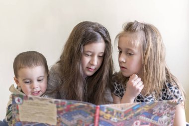 Üç küçük çocuk büyük bir kitap okuyun. İki kız ve bir erkek kardeşi. Açık renkli. Avrupa görünüm.