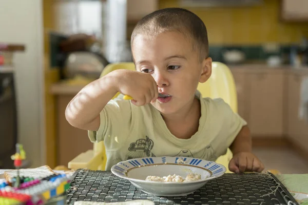 El chico de 2 años come gachas. Mesa de niños. El concepto de independencia de los niños. niño feliz comiendo gachas. Niño desayunando en la mesa — Foto de Stock