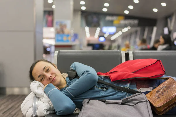 Młoda kobieta, spanie na lotnisku w oczekiwaniu na jej lotu. Zmęczony podróżny kobieta śpi na ławce airpot wylotu bramy z jej bagażu u jej boku. Tireing koncepcja podróży. z bliska — Zdjęcie stockowe