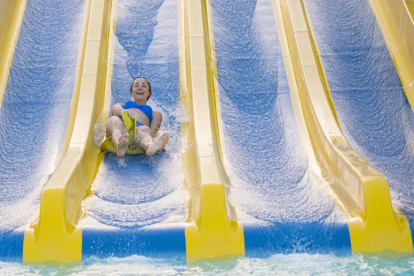 Fun in the sun-pretty girl in bikini comes down water chute in to swimming pool. Beautiful girl riding a water slide. happy woman going down on the rubber ring by the orange slide in the aqua park