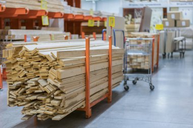 Kereste Amerika'da büyük donanım deposunun içinde raflarda yeni ahşap çubukları yığını. Taze değirmen raf ya da Ahşap ahşap Kafesli döşeme sepeti ve manuel forklift ambarı ile kesme. Müşteri alışveriş.