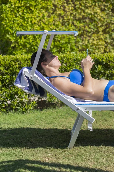 夏季生活方式的肖像年轻的惊人的女人躺在热带岛屿的海滩上的日光浴床上 年轻的白人妇女躺在蓝色的日光浴床上 躺在绿色公园的躺椅上的妇女 — 图库照片