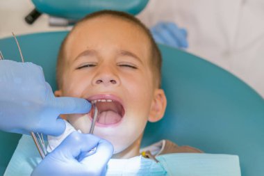 Diş hekimi bir çocuğun diş tedavi ediyor. Çocuk Diş Kliniği inceleyerek dişçi. Küçük bir hastada diş sandalye gülümsüyor. Dantist diş davranır