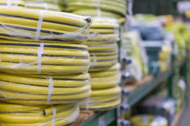 stacks of rolls yellow pvc plastic pipe on the counter in the store. Sale Hoses in the garden of various manufacturers, on shelves in store. Hose for watering in the store. clipart