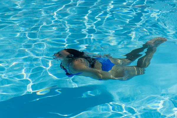 Frau mit Badeanzug schwimmt auf einem blauen Wasserbecken. Unterwasser-Frauenporträt mit blauem Bikini im Schwimmbad. — Stockfoto
