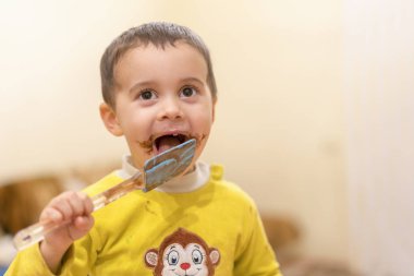 Mutlu bir çocuk bir kaşık çikolata ile yalıyor. Mutlu çocuk çikolatalı kek yeme. Komik bebek yeme çikolata bir kaşık ile.