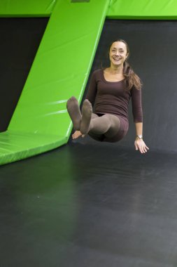 Genç kadın kahverengi uyum içinde elbise trambolin Center'da trambolin üzerinde. dikey fotoğraf. Mutlu kız trambolin üzerinde. dikey fotoğraf