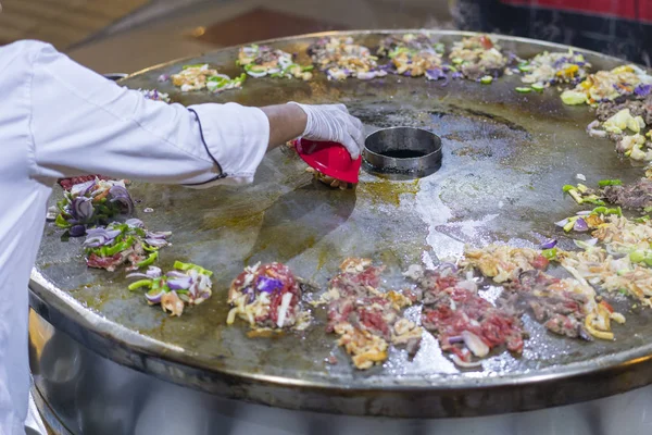 Cooking street food on a large firebox. Frying meat and seafood on the brazier in the street. A cook in a restaurant fries food on a large iron firebox