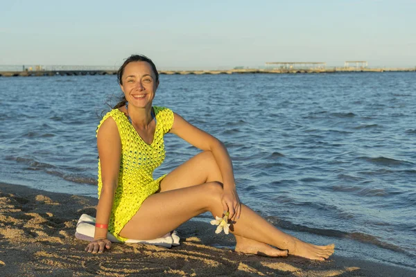 ビーチの上に座って幸せな若い女 青空屋外に対して砂浜に座っている女性 魅力的な若い女性は 彼女の膝に肘をビーチに座っています 水平ショット — ストック写真
