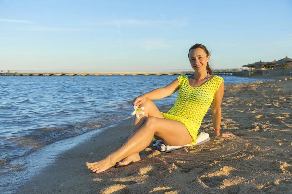 ビーチの上に座って幸せな若い女 青空屋外に対して砂浜に座っている女性 魅力的な若い女性は 彼女の膝に肘をビーチに座っています 水平ショット — ストック写真