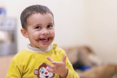 Mutlu bir çocuk bir kaşık çikolata ile yalıyor. Mutlu çocuk çikolatalı kek yeme. Komik bebek yeme çikolata bir kaşıkla. kirli mutlu çocuk