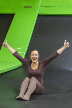 genç kadın kahverengi uyum içinde elbise trambolin Center'da trambolin üzerinde. dikey fotoğraf. Mutlu kız trambolin üzerinde. Trambolin üzerinde mutlu genç kadın. dikey fotoğraf