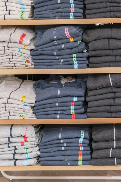 Neatly folded clothes. Rack of clothes with warm. Wooden cabinet with a stack of sweaters. Coloured clothing. Neat stacks of folded clothing on the shop shelves. vertical photo
