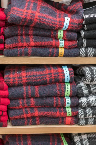 Neatly folded clothes. Rack of clothes with warm. Wooden cabinet with a stack of sweaters. Coloured clothing. Neat stacks of folded clothing on the shop shelves. vertical photo