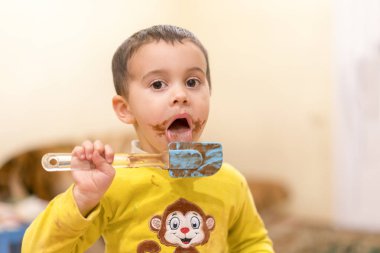 Mutlu bir çocuk bir kaşık çikolata ile yalıyor. Mutlu çocuk çikolatalı kek yeme. Komik bebek yeme çikolata bir kaşık ile