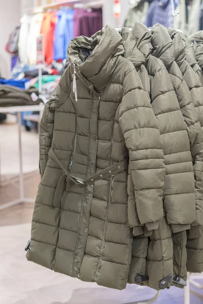 Set of clothes, coat on the rack clothing shop interior on background. Winter jackets in a store. vertical photo