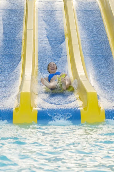 Fun in the sun-pretty girl in bikini comes down water chute in to swimming pool. Beautiful girl riding a water slide. happy woman going down on the rubber ring. vertical photo