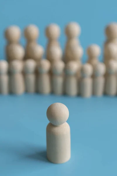 Toplum kavramı. Herkes, liderlik gibi değil kalabalıktan göze çarpıyor. Kalabalıktan dışarı ayakta. Ahşap figürler mavi bir arka plan üzerinde. dikey fotoğraf