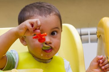 Küçük çocuk çocuk mutfakta çocuk masasında yemeye öğrenir. Komik bebek yiyor. Küçük bebek ile bir kaşık çorba plaka yiyor. Gıdalar koyarak bir çocuk sandalyede oturuyor.
