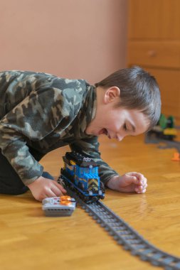 Küçük çocuk bir oyuncak tren ile oynuyor. Yerde yatarken demiryolu ile oynarken küçük çocuk. Neşeli duygular. dikey fotoğraf.
