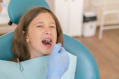 Küçük kız dişçi ofisinde resepsiyonda. sonra diş tedavileri diş hekimi yakın bir sandalyede oturan küçük kız. Dişçi ofisinde küçük kız sitts.