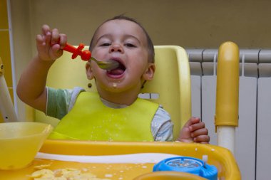 Küçük çocuk çocuk mutfakta çocuk masasında yemeye öğrenir. Komik bebek yiyor. Küçük bebek ile bir kaşık çorba plaka yiyor. Gıdalar koyarak bir çocuk sandalyede oturuyor.