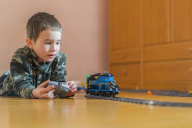 Küçük çocuk bir oyuncak tren ile oynuyor. Küçük çocuk yerde yatarken demiryolu ile oynarken.