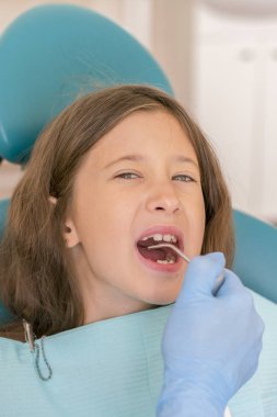 Küçük kız dişçi ofisinde resepsiyonda. sonra diş tedavileri diş hekimi yakın bir sandalyede oturan küçük kız. Küçük kız sitts dişçi ofisinde. dikey fotoğraf